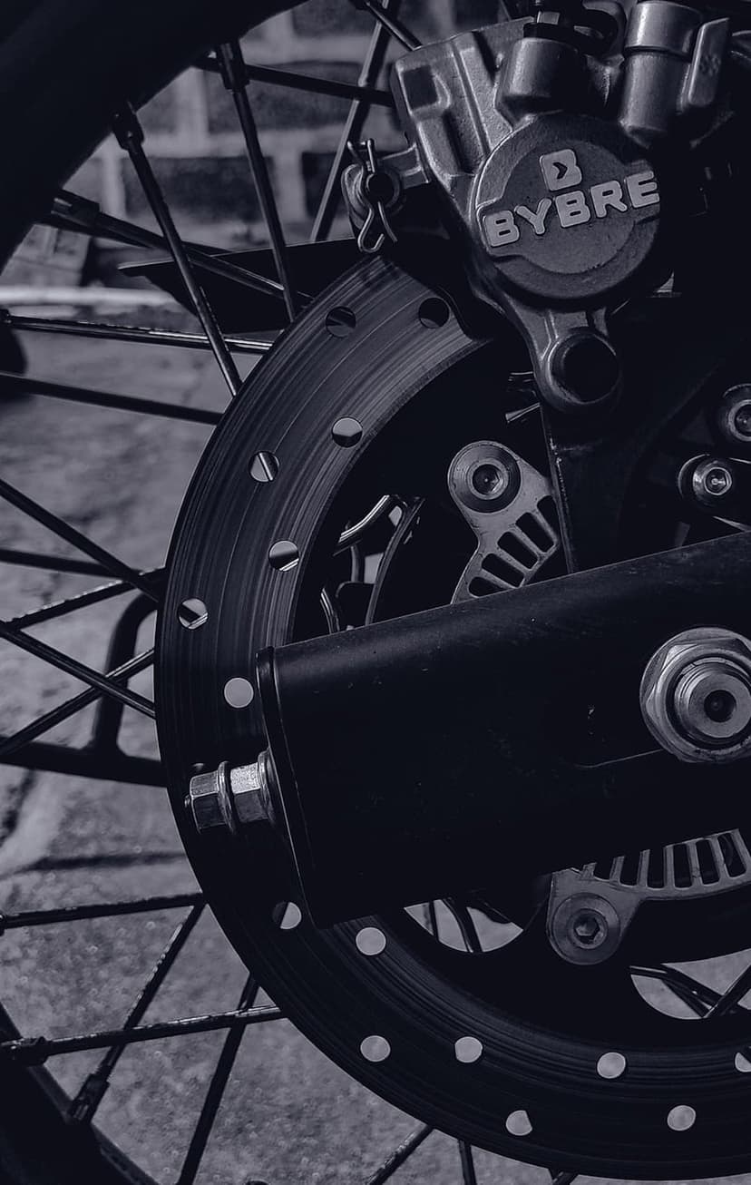 Rear brake disc and BYBRE caliper in monochrome showing drilled metal textures and rugged mechanical bike parts.