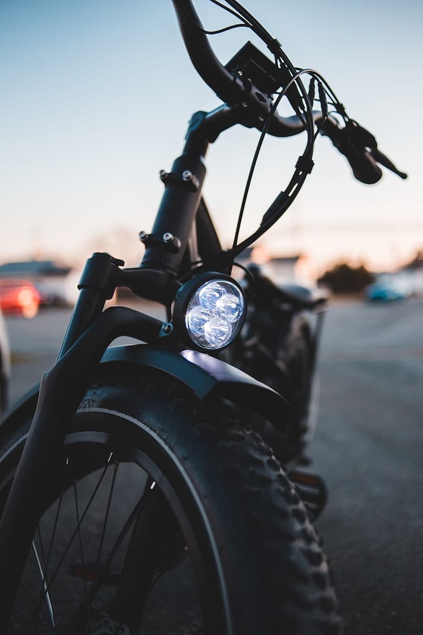 Black fat tire electric bike front wheel and multi-LED headlight with handlebars against a soft-focus sky.