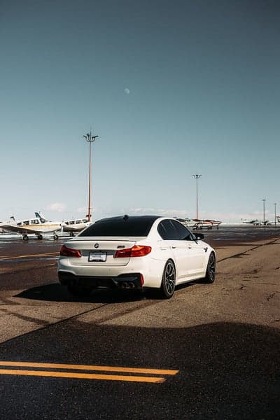 White BMW M5 on airport tarmac with small planes