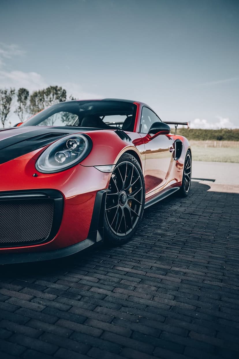 Red Porsche 911 GT2 RS with black stripes on a brick road under a clear sky, featuring a large rear wing and spoiler.