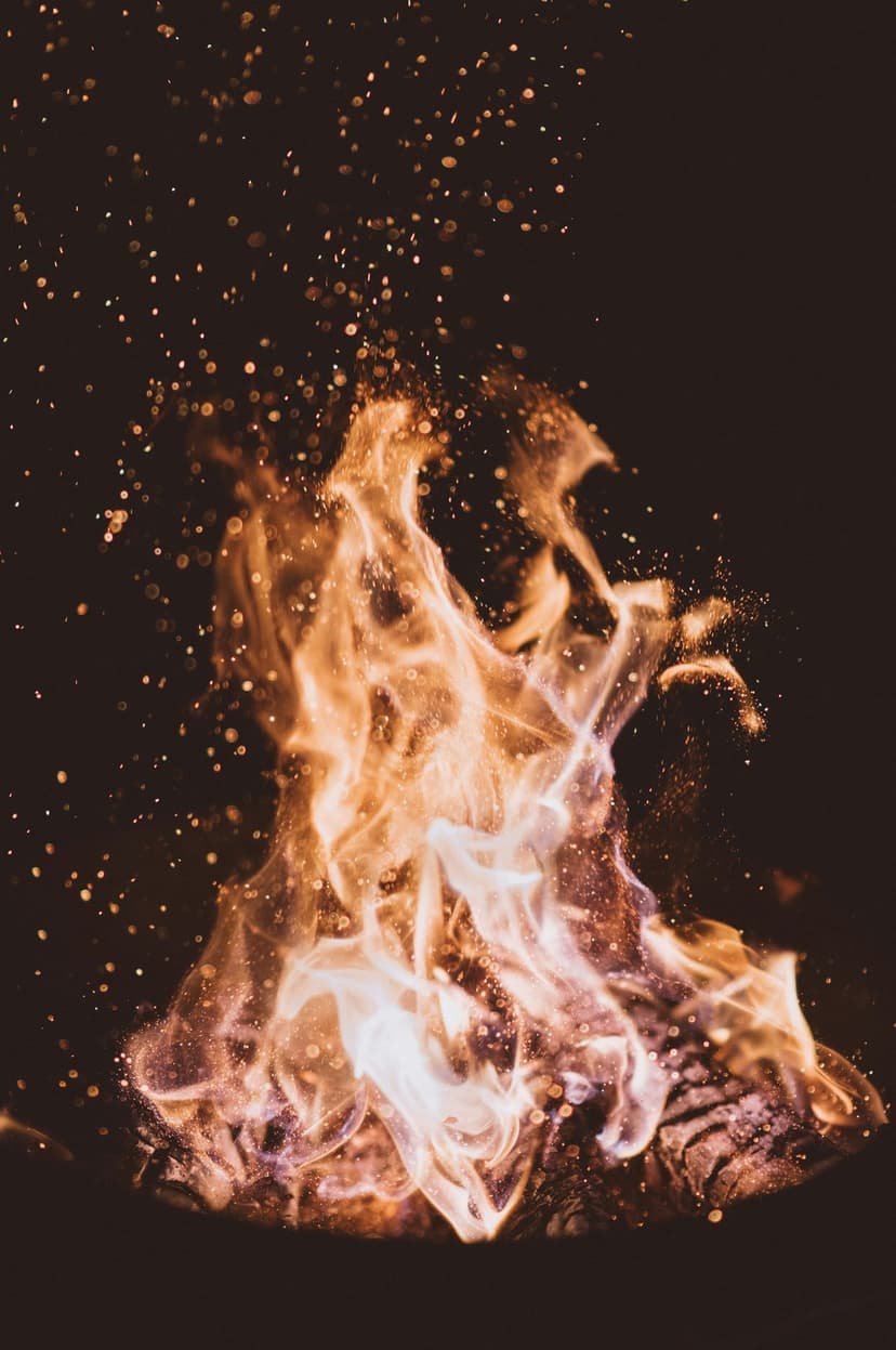 Bright orange flames and white-hot embers swirl against a black background with glowing sparks and heat waves.