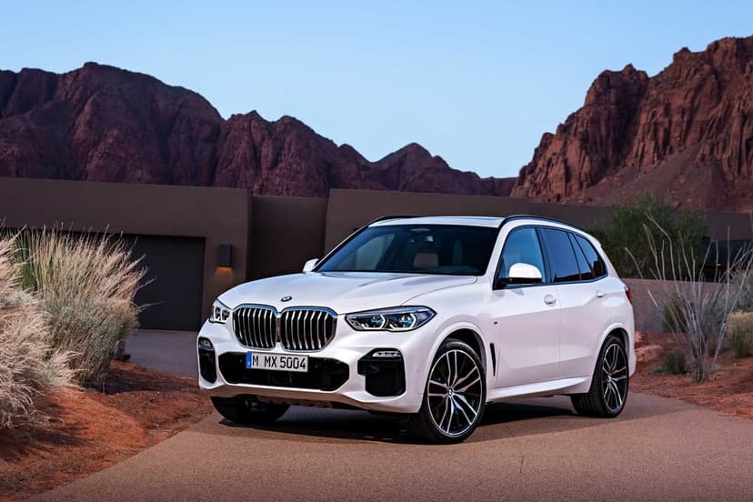 White luxury SUV parked on a road with red desert mountains and a modern house under a clear sky.