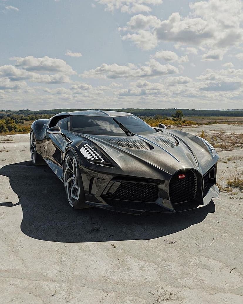 Bugatti Centodieci hypercar in metallic gray parked on a dusty landscape under a soft blue sky with clouds.