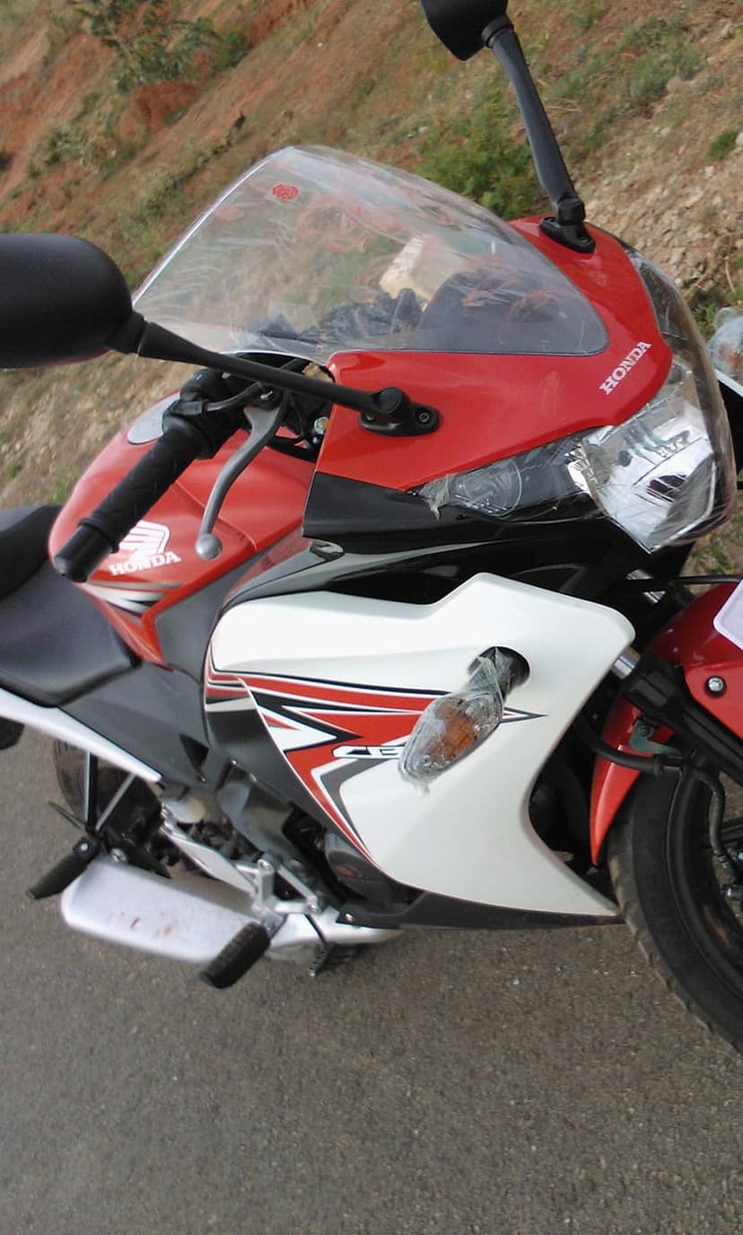 Honda CBR motorcycle with red fairing graphics and clear windshield parked on asphalt against blurred hills.