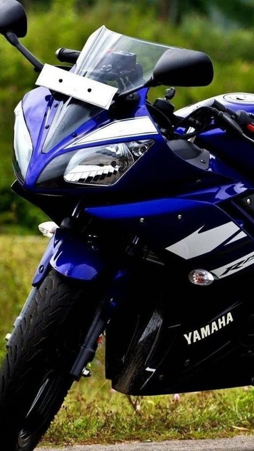 Blue Yamaha R15 motorcycle front view showing sharp headlights and a windshield against a blurred green field.