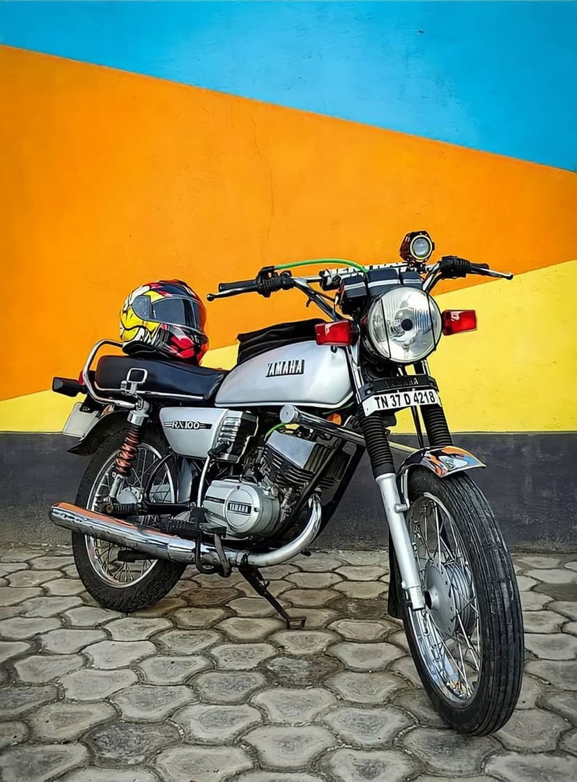 Yamaha RX 100 vintage motorcycle with a helmet on its seat against a bright orange and blue segmented wall.