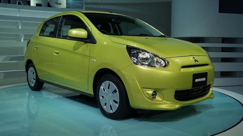 Lime green Mitsubishi Mirage hatchback on a glossy display stand with studio lighting in a showroom.