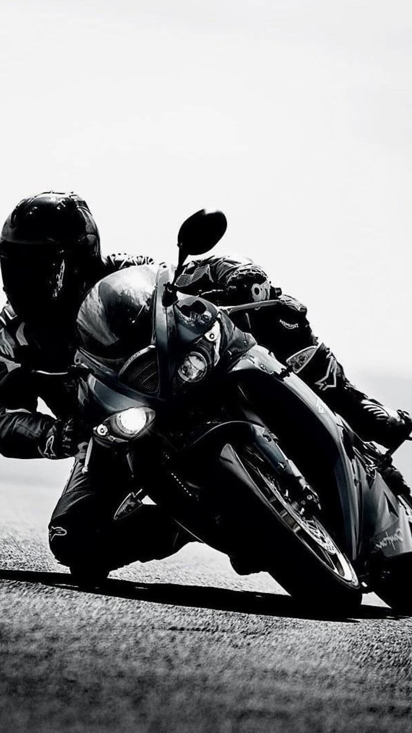 Professional motorcyclist in a dark racing suit leans into a sharp turn on a track with glowing headlights.
