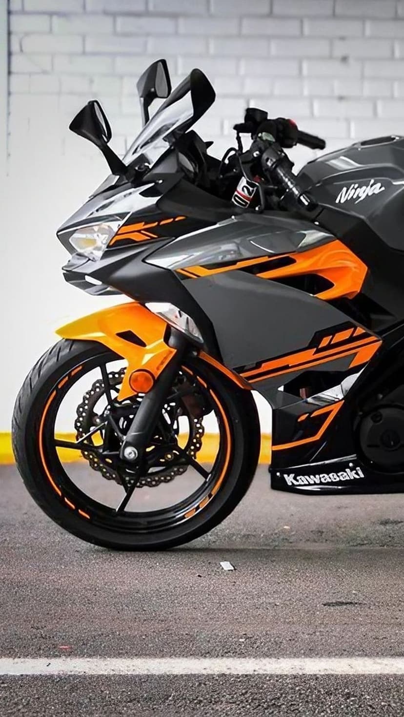 Kawasaki Ninja motorcycle with orange accents and gray fairings against a white brick wall in a close-up view.