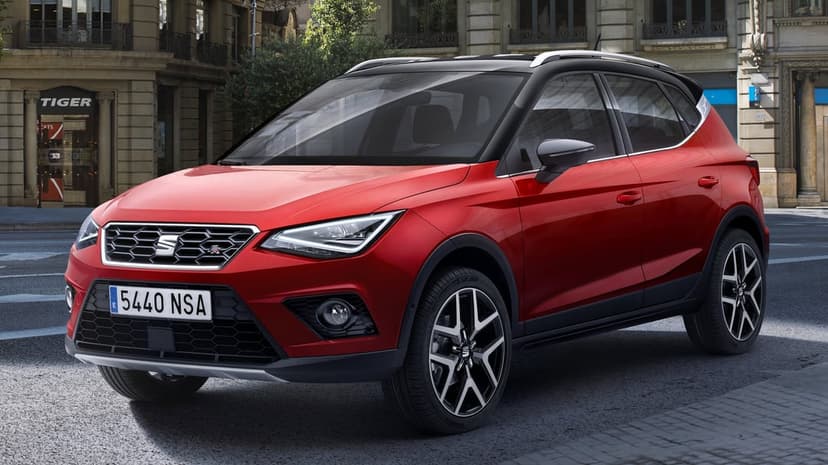 Red SEAT Arona SUV with a black roof parked on a city street in front of stone buildings and a storefront.