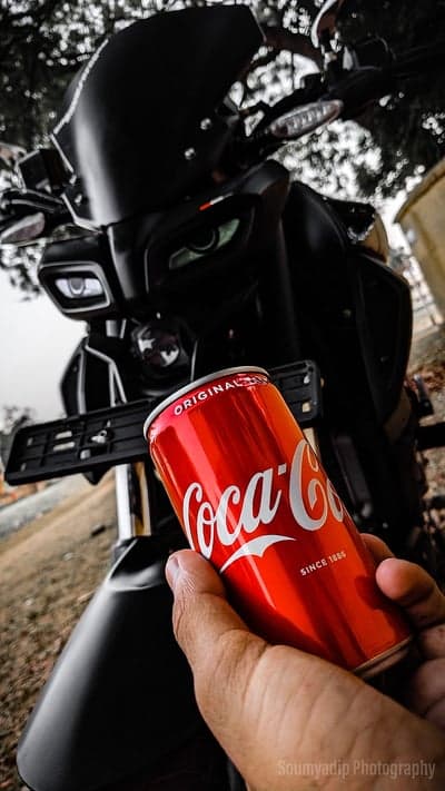 Hand holding Coca-Cola can in front of motorcycle