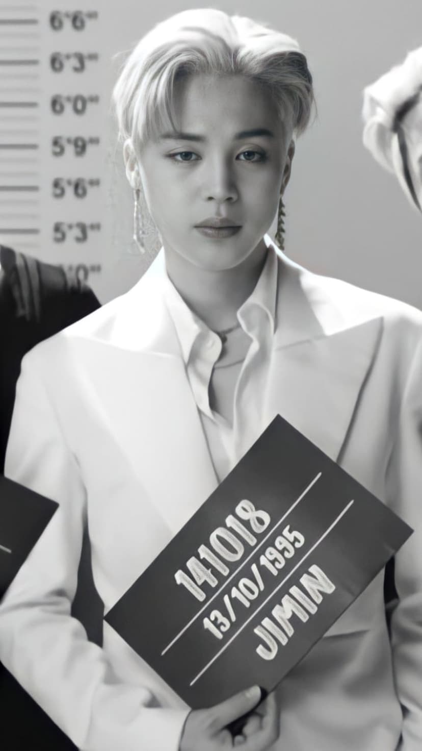 Jimin holds a police mugshot board in front of a height chart while wearing a white suit in monochrome.