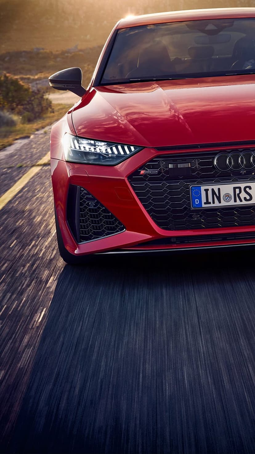 Red Audi RS7 sportback speeding on a rural highway at sunset with motion blur and glowing LED headlights.