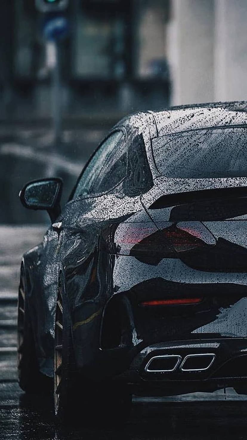 Black sports car rear view featuring glowing red taillights and rain droplets on a wet city street.