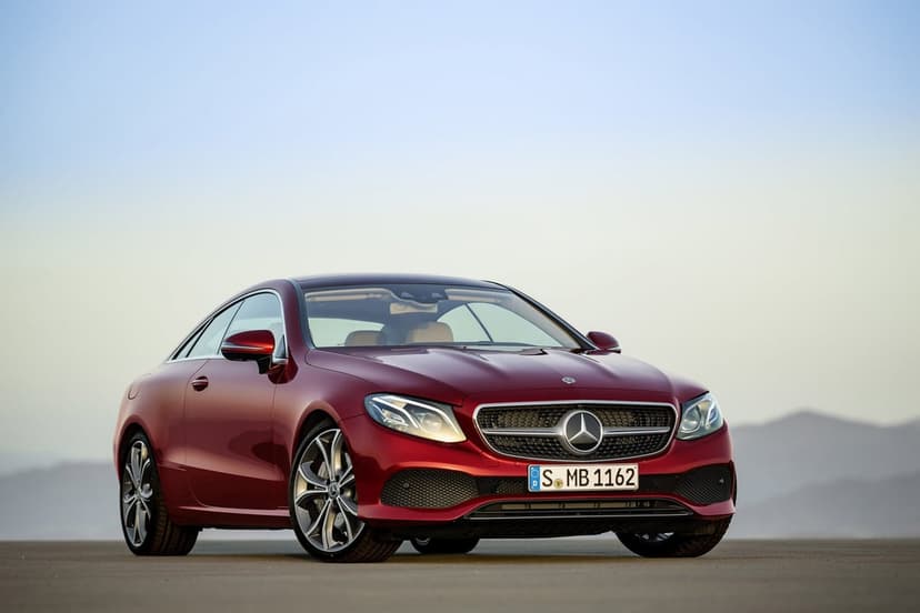 Red Mercedes-Benz E-Class Coupe parked on a flat surface against a soft blue and orange gradient dusk sky.