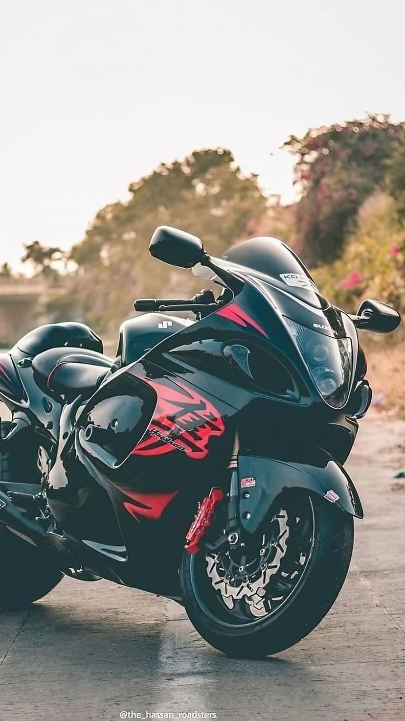 Black Suzuki Hayabusa motorcycle with red fairing accents parked outdoors against a blurred foliage background.