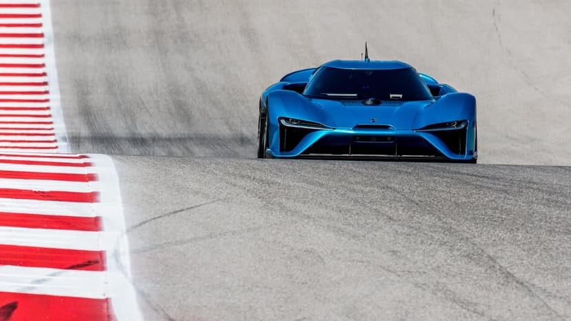 Blue electric supercar centered on a grey racetrack with red and white striped curbs under bright daylight.