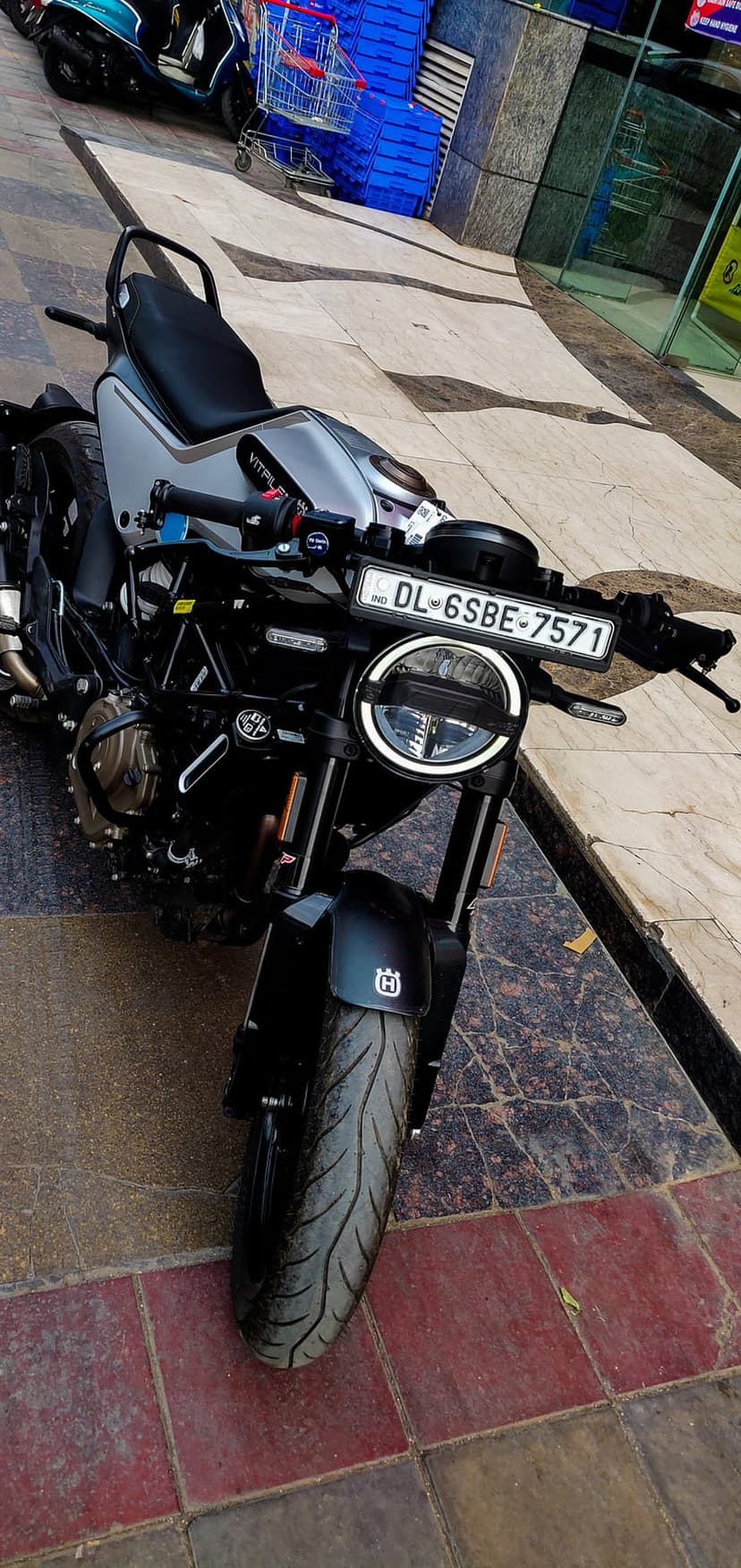 Husqvarna Vitpilen 250 motorcycle with a round LED headlight parked on a gray tiled sidewalk in an urban setting.