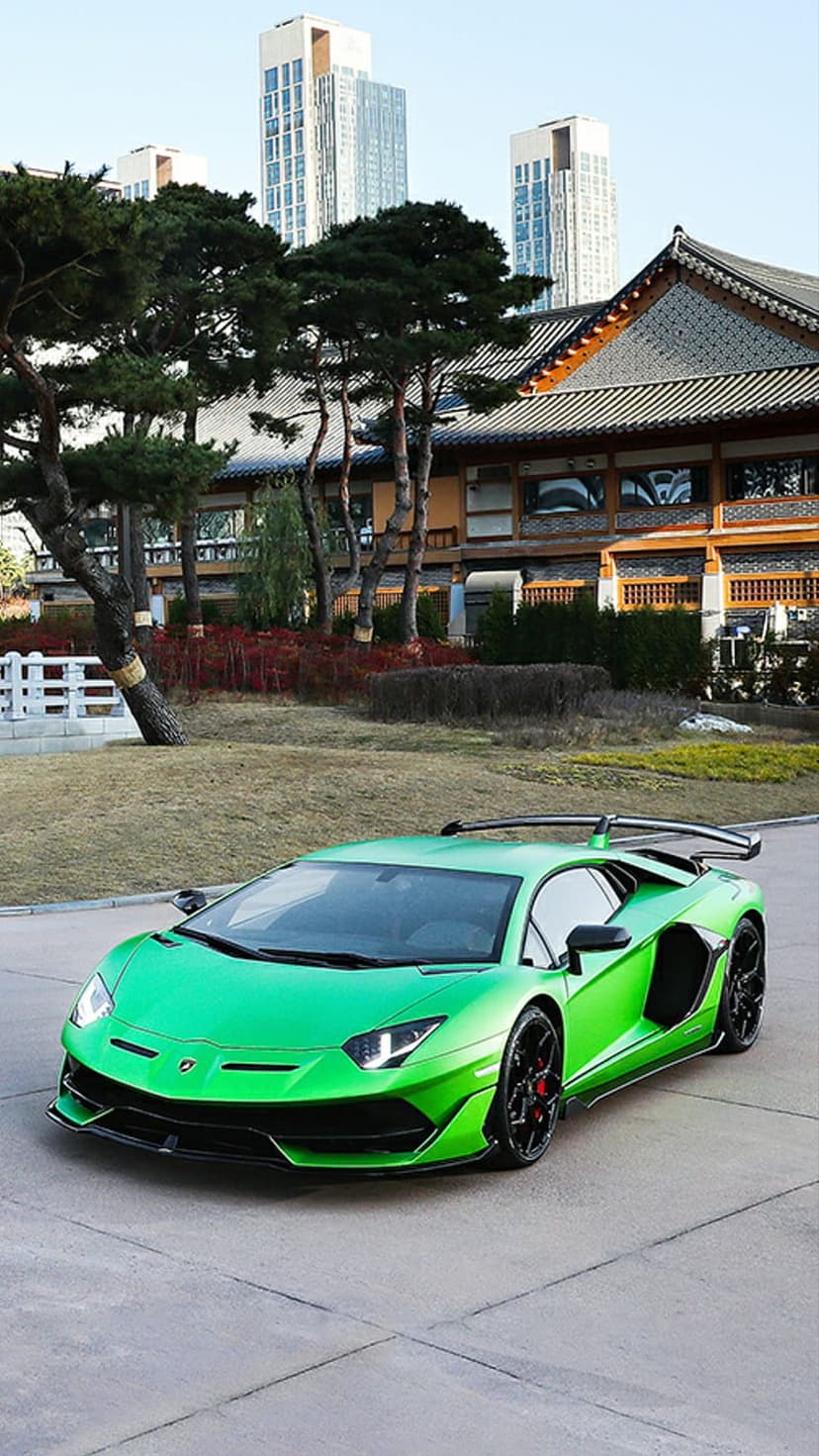 Lime green Lamborghini Aventador SVJ parked before a traditional Korean house with distant modern skyscrapers.