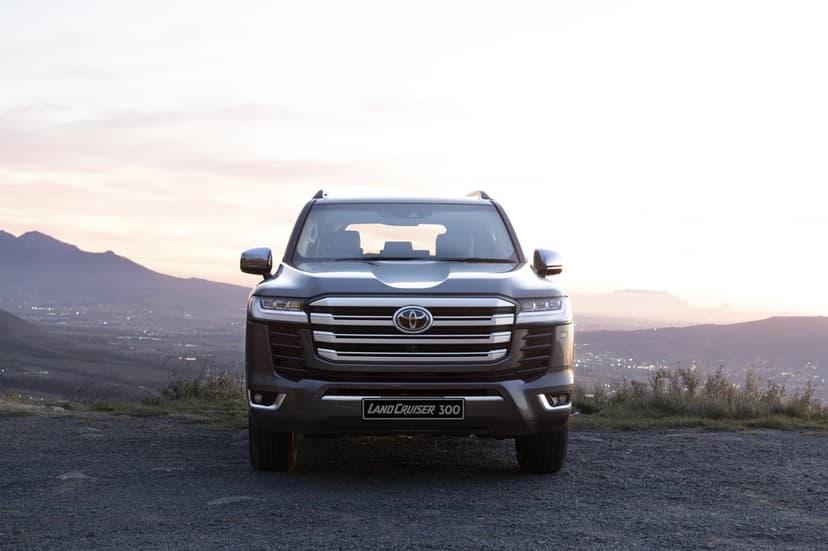 Toyota Land Cruiser 300 centered on a gravel ridge against a soft sunset sky and distant mountain valley.