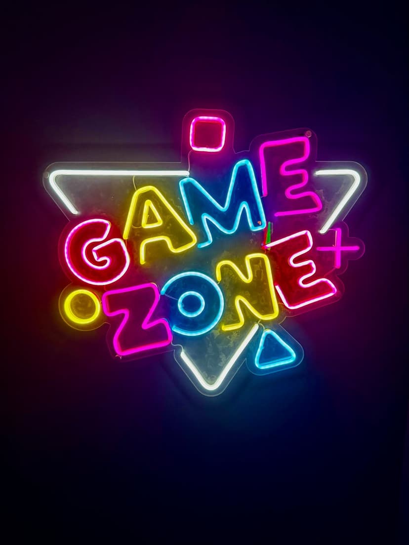 Game Zone sign glows in neon blue and pink letters with geometric outlines against a dark black background.