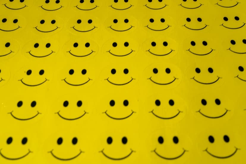 Yellow smiley face stickers with black eyes and curved mouths form a repeating pattern on a bright background.