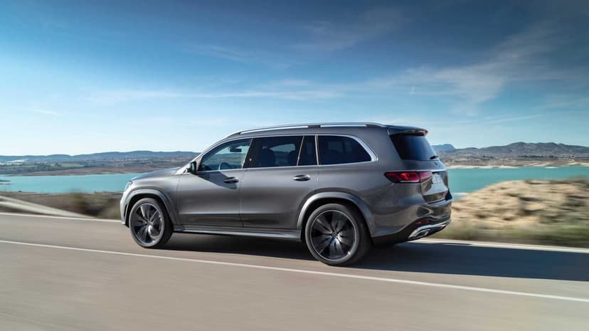Grey luxury SUV driving along a winding coastal road with blue water and mountains under a bright sky.