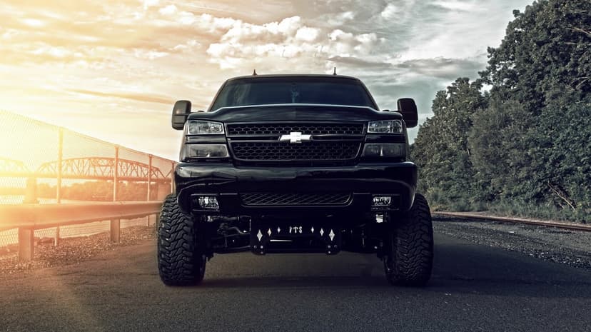 Black lifted Chevrolet Silverado truck with large off-road tires parked on a road at sunset near a bridge.