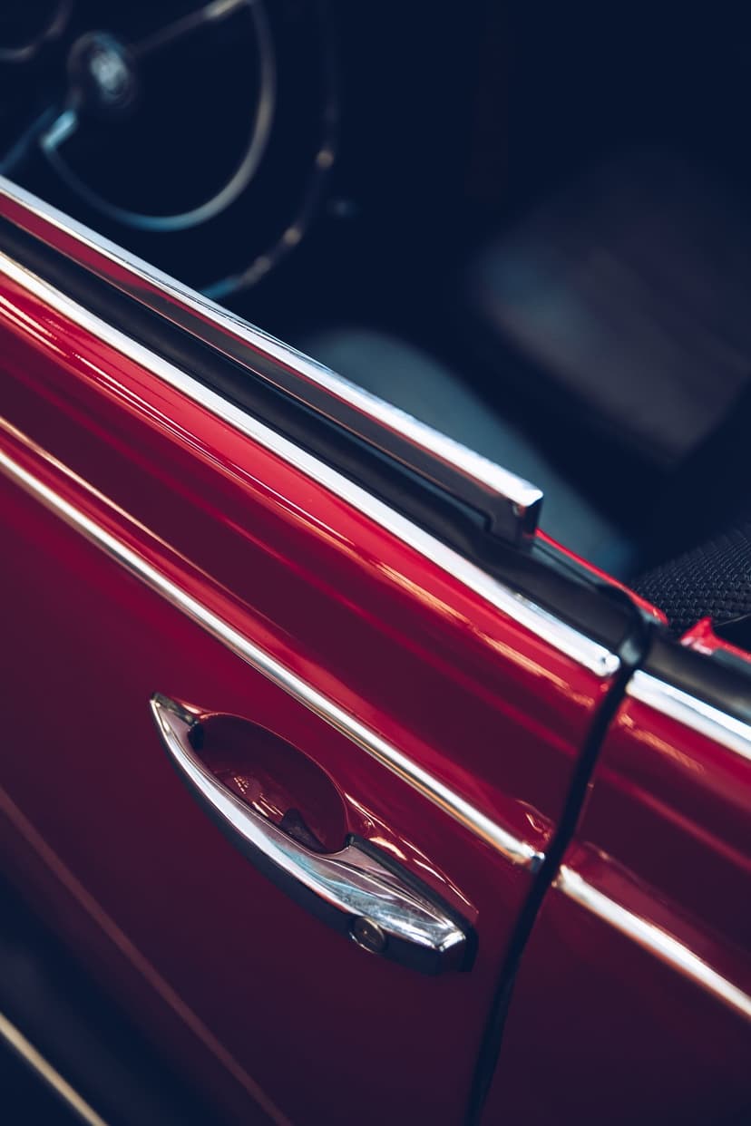 Vintage red car door featuring a polished silver handle, sleek automotive paint, and a glimpse of the interior.