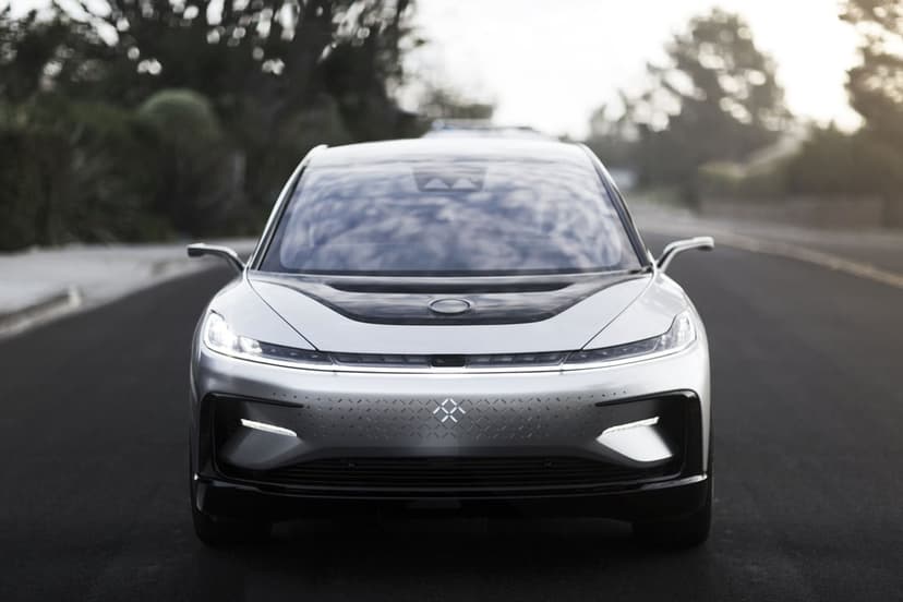 Front view of a silver Faraday Future FF 91 electric car on a paved road with slim LED lights and camera mirrors.
