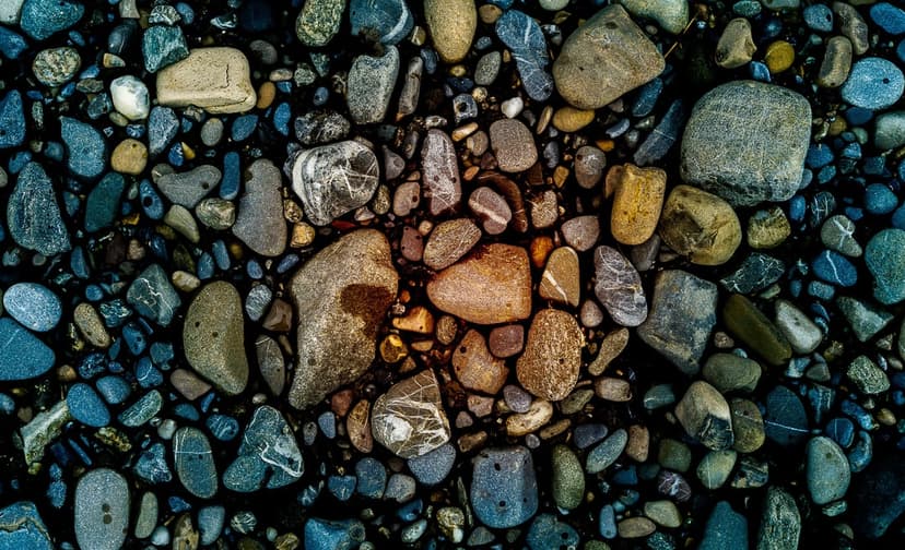Smooth wet river rocks in shades of blue, brown, and yellow create a dense, textured natural mosaic pattern.