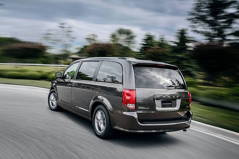 Rear view of a dark brown Dodge Grand Caravan minivan driving fast on a curved asphalt road with motion blur.