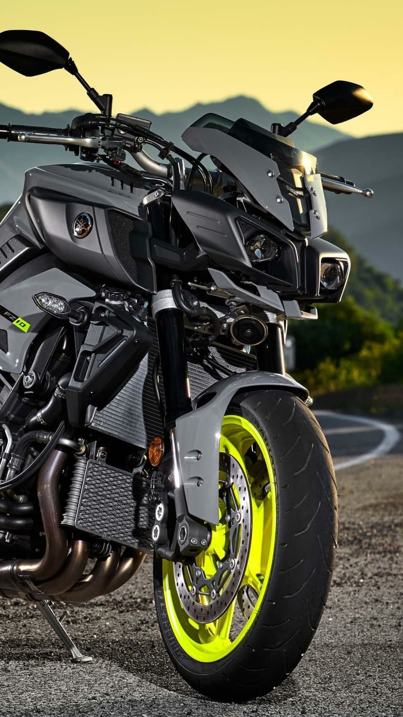 Yamaha MT-10 motorcycle with grey bodywork and neon yellow wheels against a blurred sunset mountain landscape.
