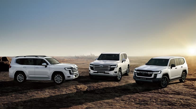 Three white Toyota Land Cruiser SUVs parked on a rocky desert plateau under a golden sunrise sky with a distant city.