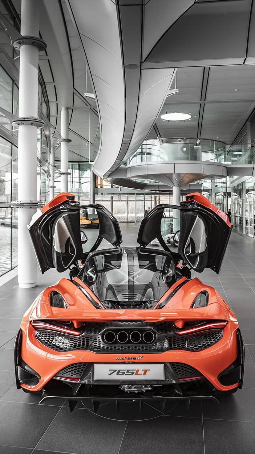 McLaren 765LT supercar in orange with butterfly doors open in a bright showroom featuring a quad exhaust system.