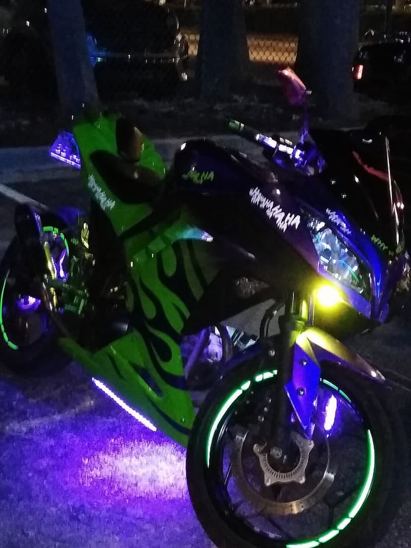 Custom sportbike featuring neon green flame decals and blue LED underglow glows against a dark night backdrop.