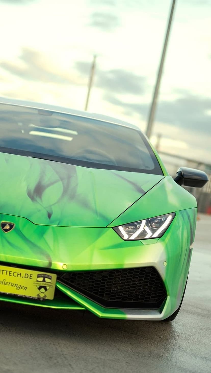 Green Lamborghini Huracan with custom flame graphics, sharp headlights, and a black honeycomb front grille.