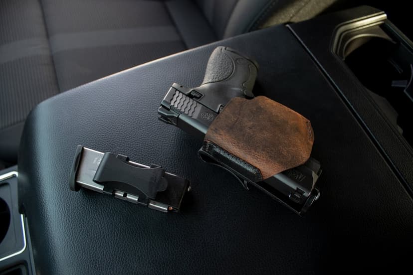Black handgun in a brown leather holster sits next to a loaded magazine on a dark car interior center console.