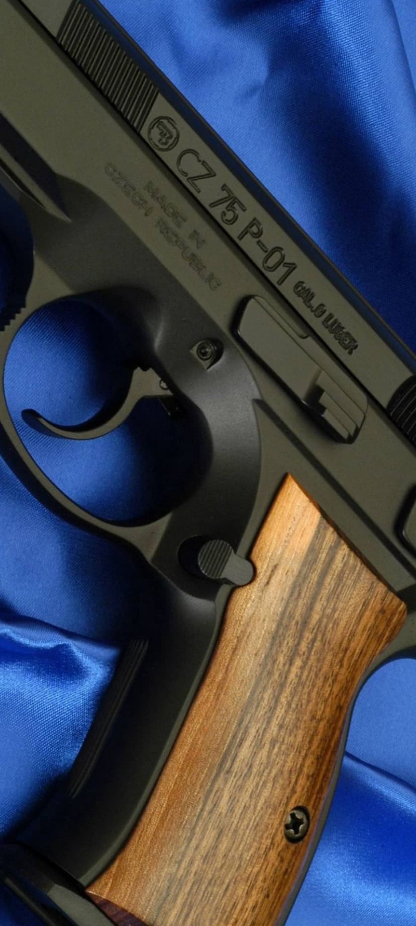 CZ 75 P-01 pistol with textured wood grips rests on a draped royal blue cloth with soft lighting reflections.