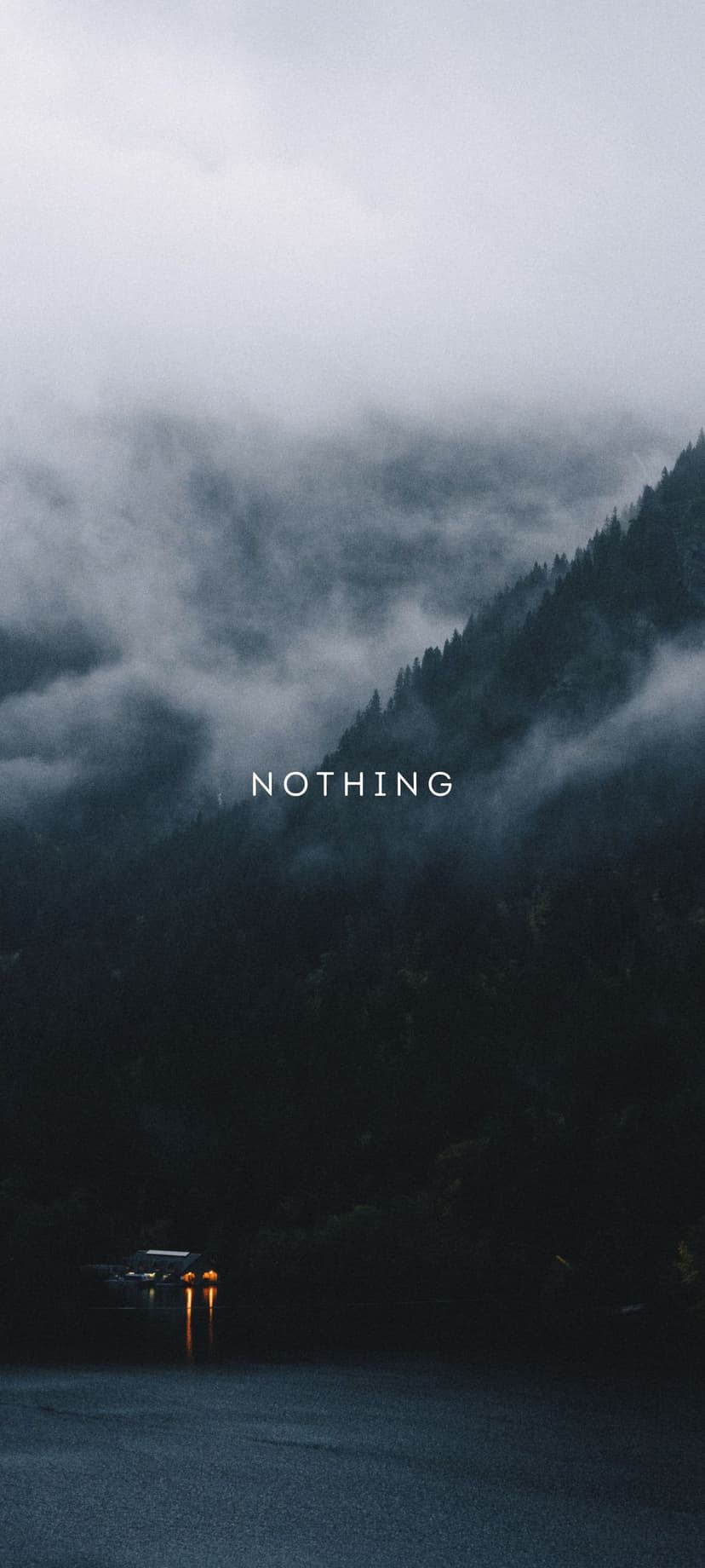 Foggy evergreen mountains rise above dark water with white Nothing text overlaid on the misty landscape.