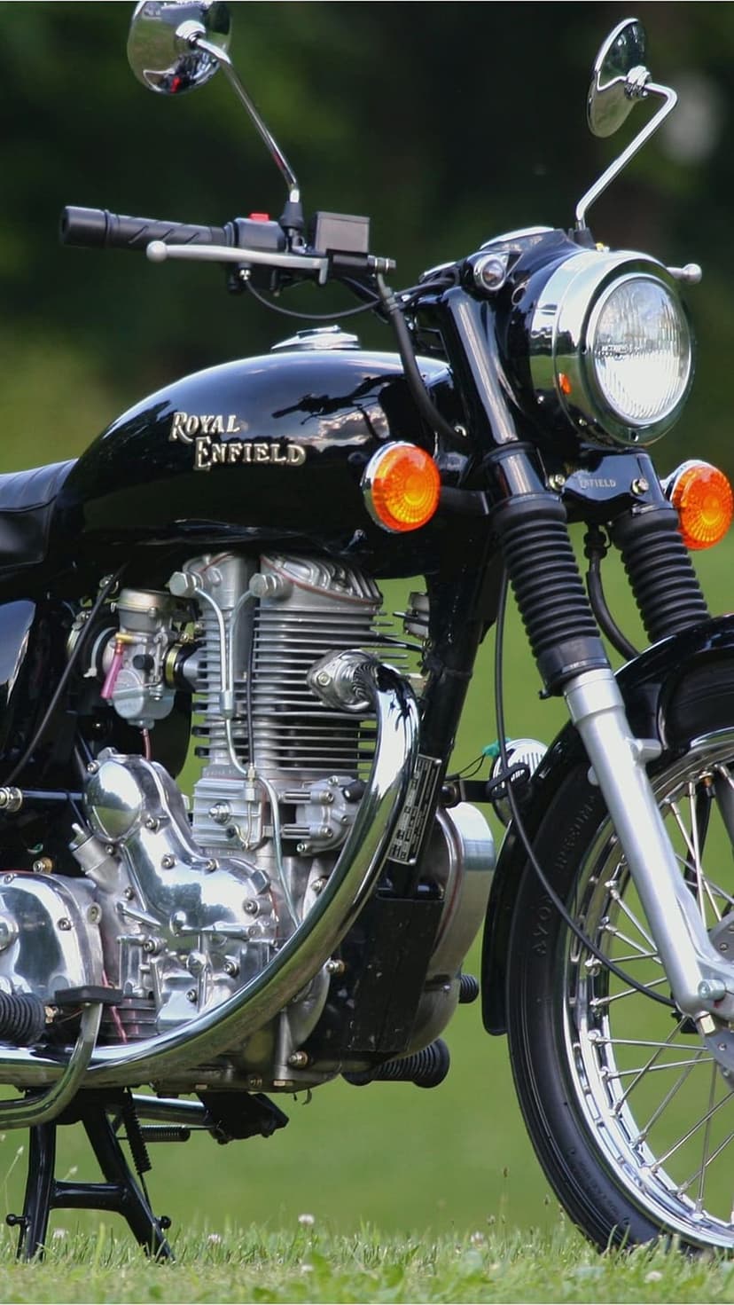 Black Royal Enfield motorcycle with chrome engine parts parked on vibrant green grass in a vertical composition.