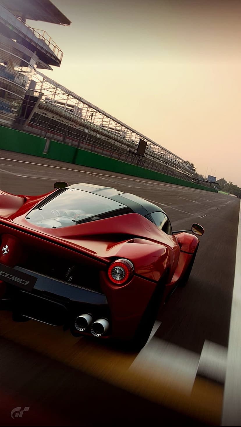 Red Ferrari supercar racing on a track at sunset with glowing taillights and blurred grandstands behind.