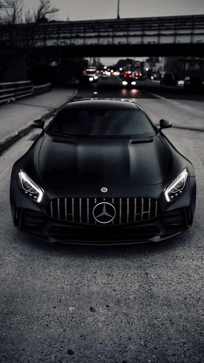 Black Mercedes-AMG GT S sits on a city street at night with glowing headlights and a blurred urban background.