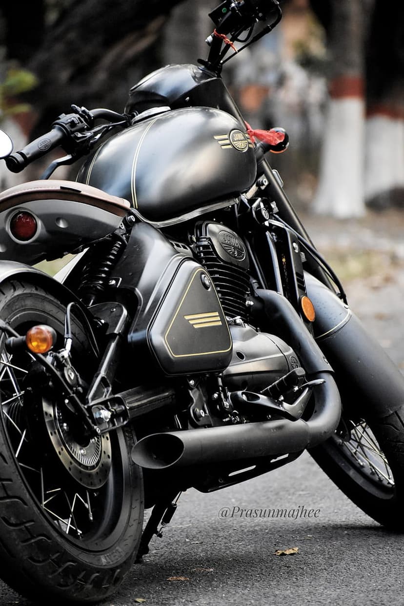 Matte black Jawa motorcycle engine and fuel tank with chrome details parked on a textured asphalt road.