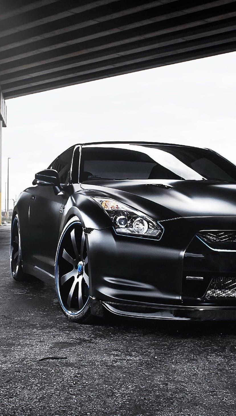 Nissan GT-R with blue wheel accents parked on asphalt under a concrete structure with reflections on black paint
