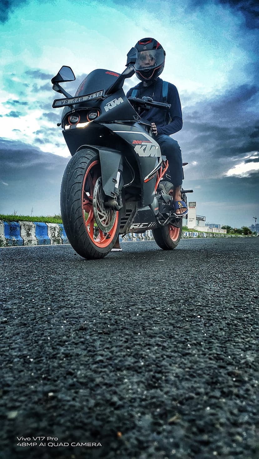 KTM rider wearing a helmet sits on a black motorcycle with orange rims beneath a dark and stormy dramatic sky.
