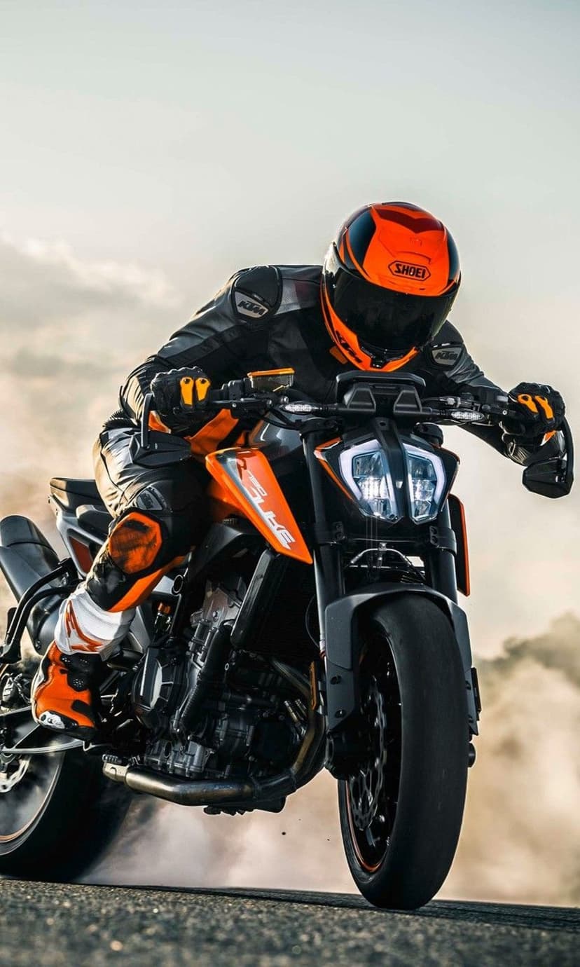 KTM motorcycle rider leaning into a sharp drift with thick white smoke billowing from the rear tire on asphalt.