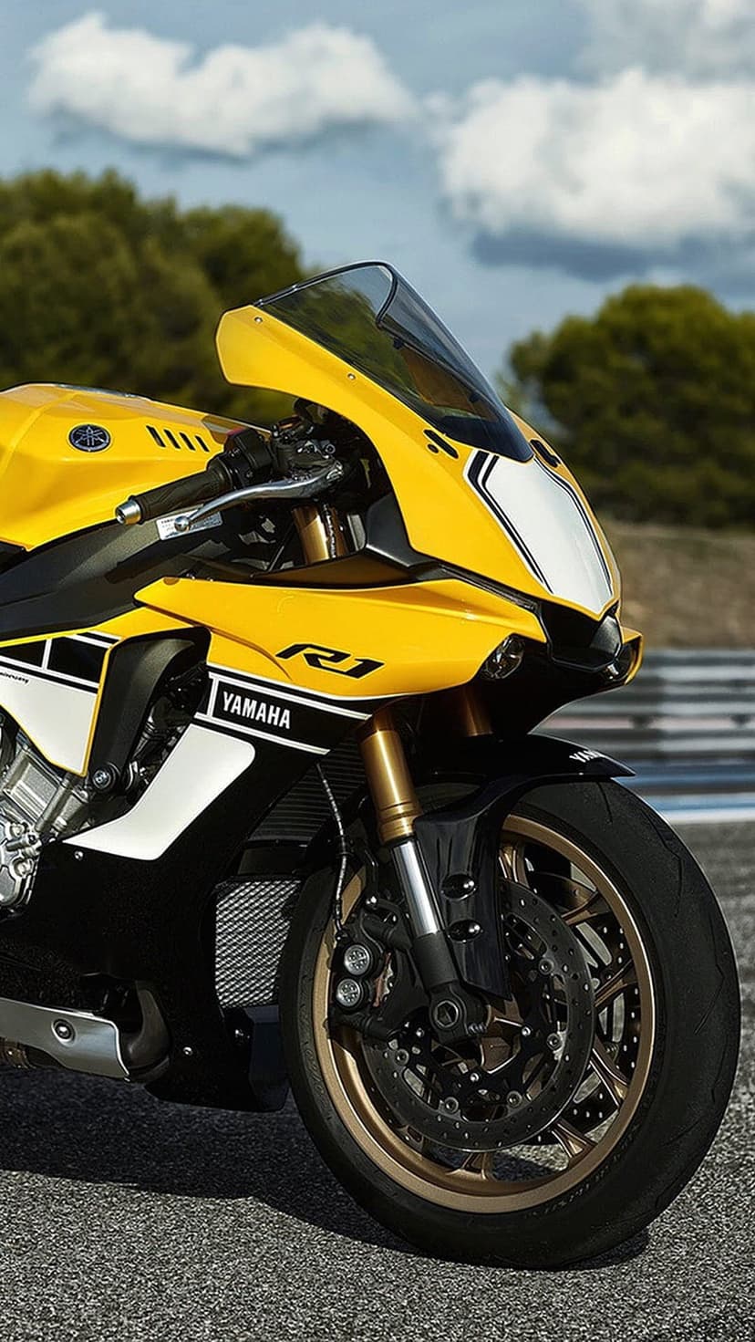 Yellow Yamaha R1 motorcycle with gold suspension parked on a grey asphalt race track under a cloudy sky.