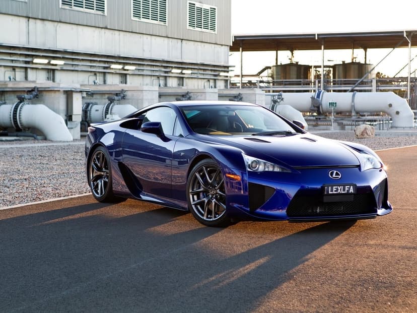Deep blue Lexus LFA parked at an industrial site during sunset with golden light reflecting on its sleek body.