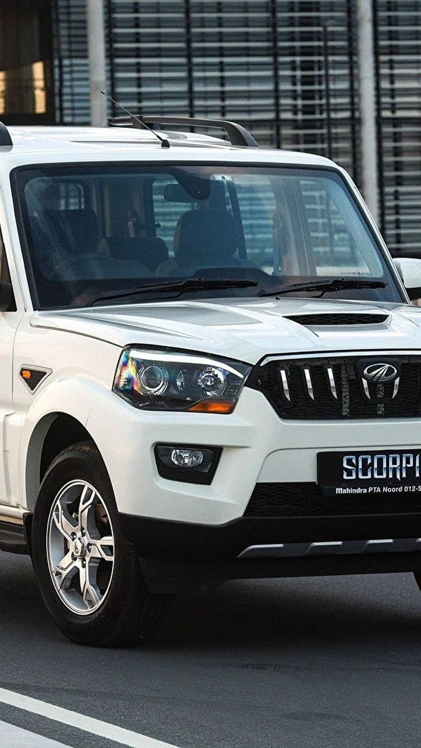 White Mahindra Scorpio SUV showing a chrome grille and headlights against a modern glass building background.